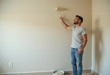 Appliquer l’apprêt avec un rouleau : astuces et conseils pratiques Homme en vêtements décontractés appliquant une sous-couche sur un mur intérieur